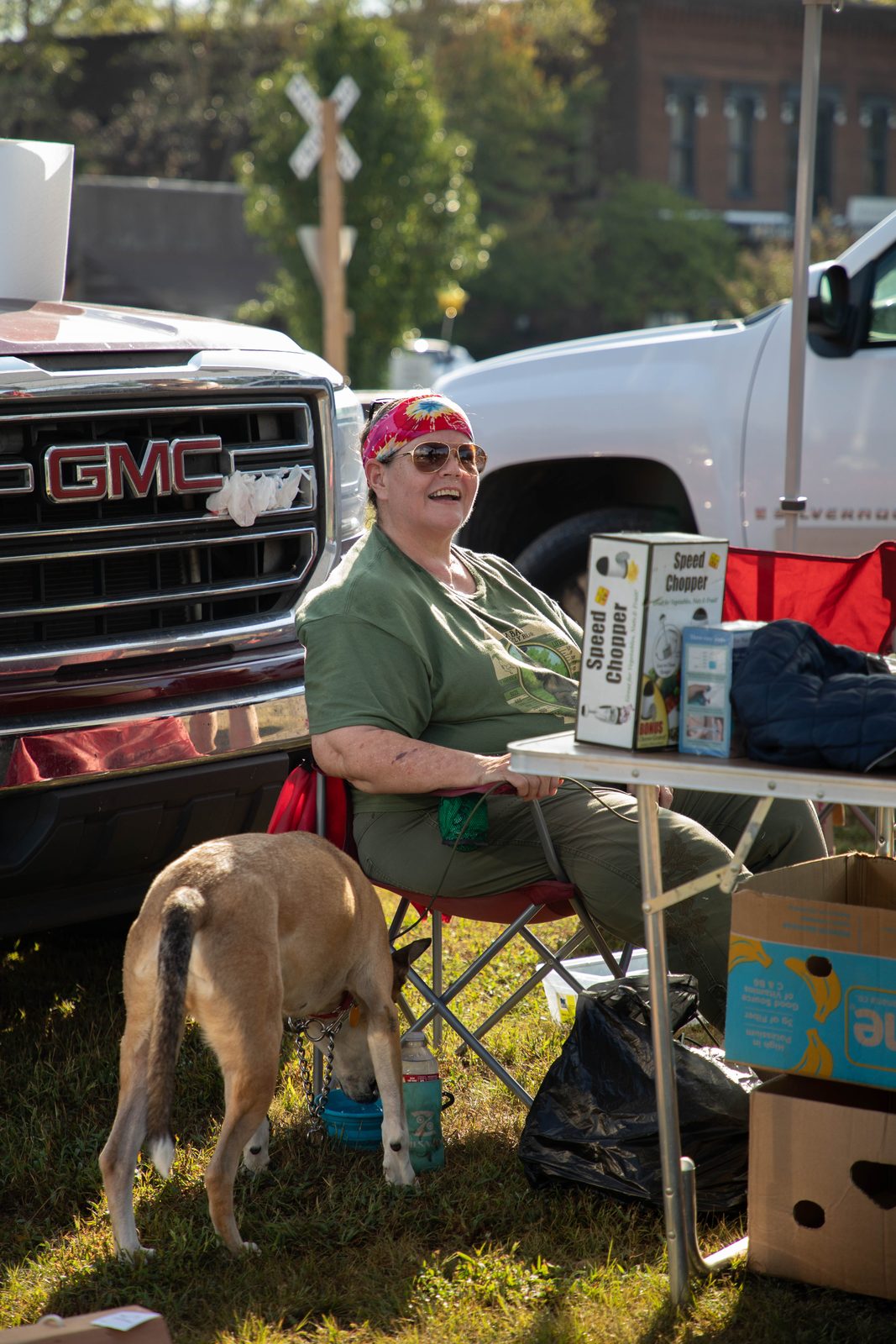 Vendor laughing hard while her dog drinks from a bowl under her chair